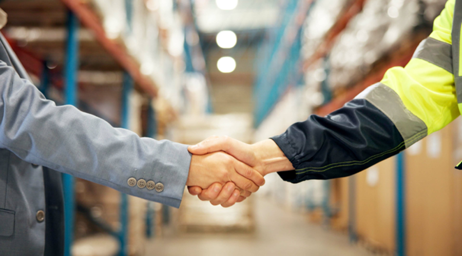 "A business professional and warehouse worker shaking hands inside a warehouse, symbolising supply chain partnership and collaboration.alt="A business professional and warehouse worker shaking hands inside a warehouse, symbolising supply chain partnership and collaboration."